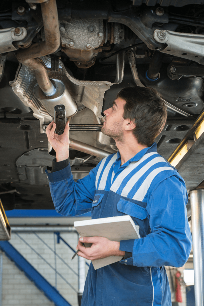 Mechanic with a torch whilst inspecting underneath a vehicle during its MOT test - MOT Testing Bathgate